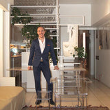 A man in a navy blue suit and white shirt stands in a Modernist interior with a Picasso sculpture and Paul Rudolph designed acrylic chair 