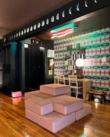 A modern interior space with a modular seating unit in the foreground, neon light fixture on the ceiling, patterned wallpaper with dark ceilings