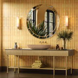 Bathroom vanity with round mirror, sink, and decorative items against a gold tiled wall.